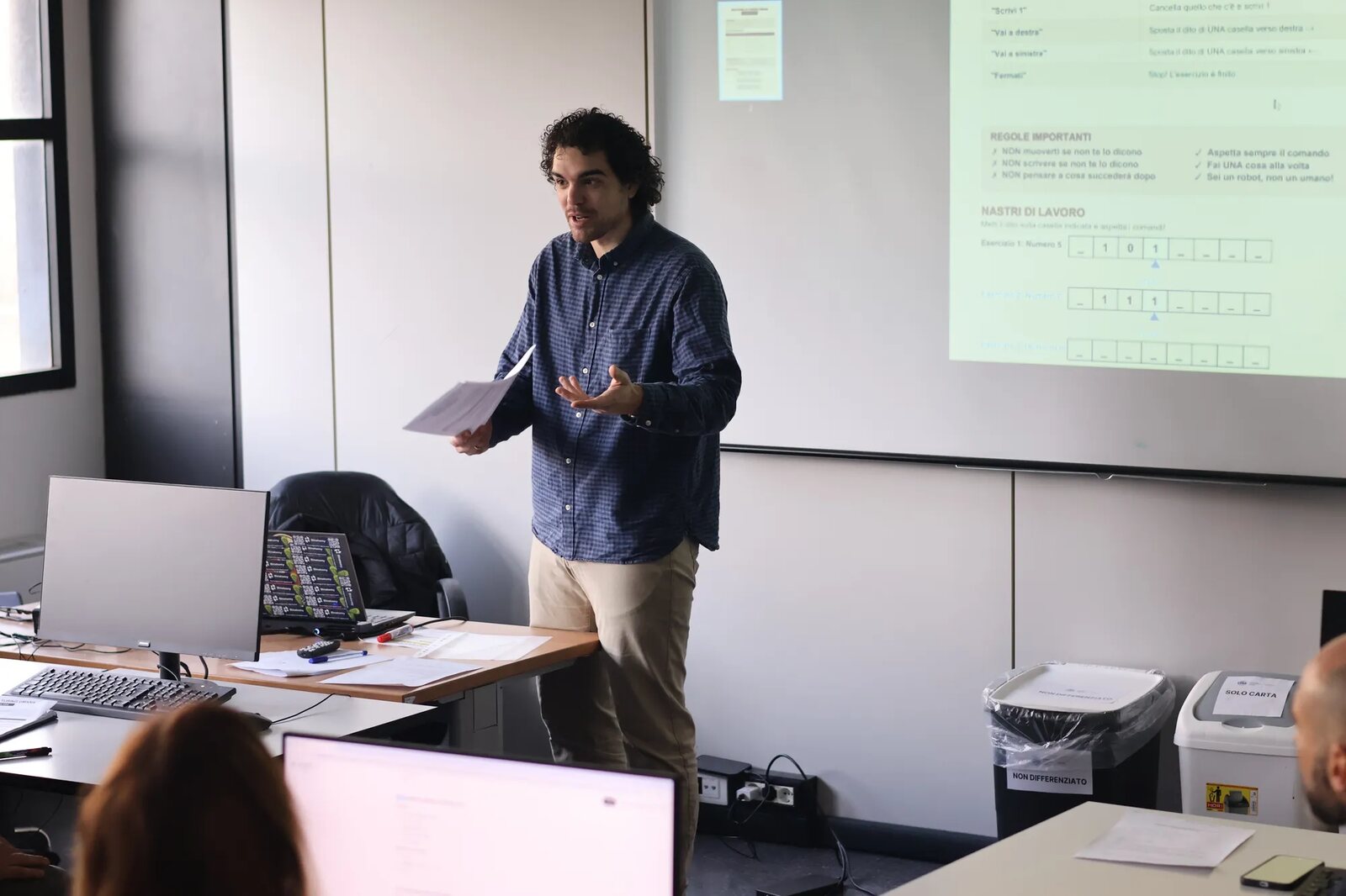 Un docente spiega davanti allo schermo durante un corso, con i partecipanti ai portatili