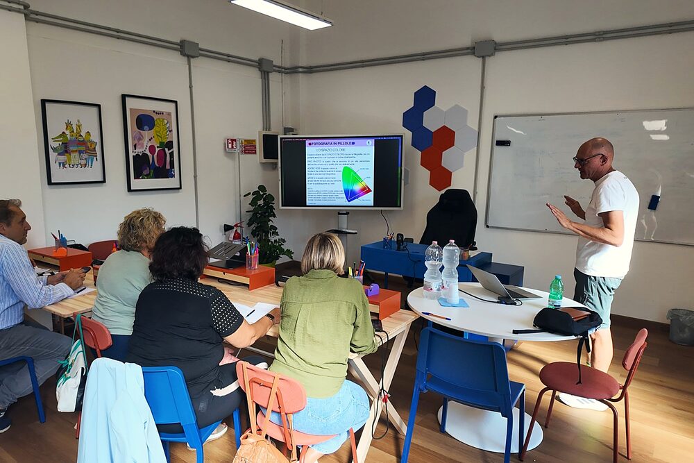 L'aula in uso durante un workshop: i partecipanti ai tavoli a isole, lo schermo acceso e chi parla accanto alla lavagna bianca
